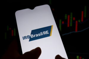 Tela de celular com logo do IRB, gráfico de ações do IRB ao fundo