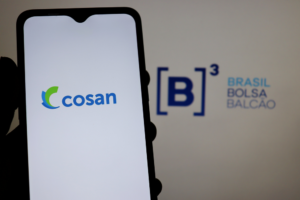 Foto de celular com logo da Cosan na tela, logo da B3 ao fundo