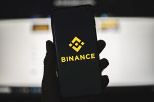 Mão segurando celular com logo da Binance