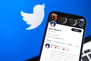 tela de celular exibe a conta do empresário Elon Musk no Twitter e, ao fundo, outra tela mostra o logotipo do Twitter