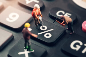 Frente de uma calculadora com "bonecos" simulando trabalhadores realizando obras na tecla de percentual.