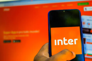 Celular com logo do banco Inter e site no fundo