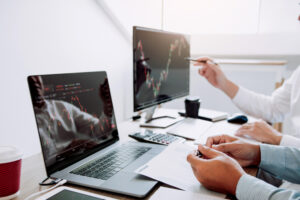 Homens trabalhando em frente a computadores com gráficos de cotação de ativos financieros