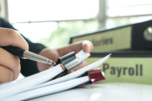 Mão segurando bloco e pasta com a palavra payroll