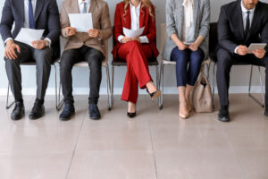Pessoas sentadas em cadeira revisando currículos à espera de emprego.