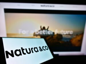 Celular com logo da Natura com tela de computador ao fundo