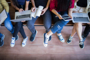 Imagem recortada de estudantes sentados como computadores na mão.