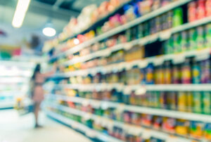 Foto desfocada de prateleiras de supermercado e pessoa fazendo compras