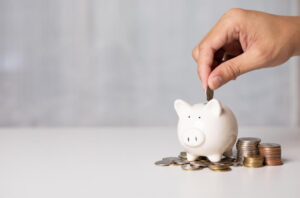 Mão colocando moedas em um cofre de porquinho