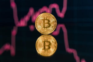 Duas moedas de Bitcoin com gráfico em queda no fundo