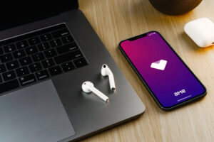 Celular com aplicativo da Ame Digital aberto, ao lado de computador e par de fones de ouvido