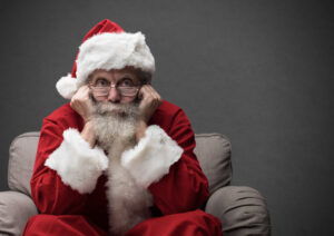 homem vestido de papai noel com feição triste sentado em uma poltrona