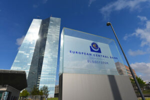 Fachada do Banco Central Europeu, com prédio espelhada à direita e placa com o nome da instituição à esquerda.